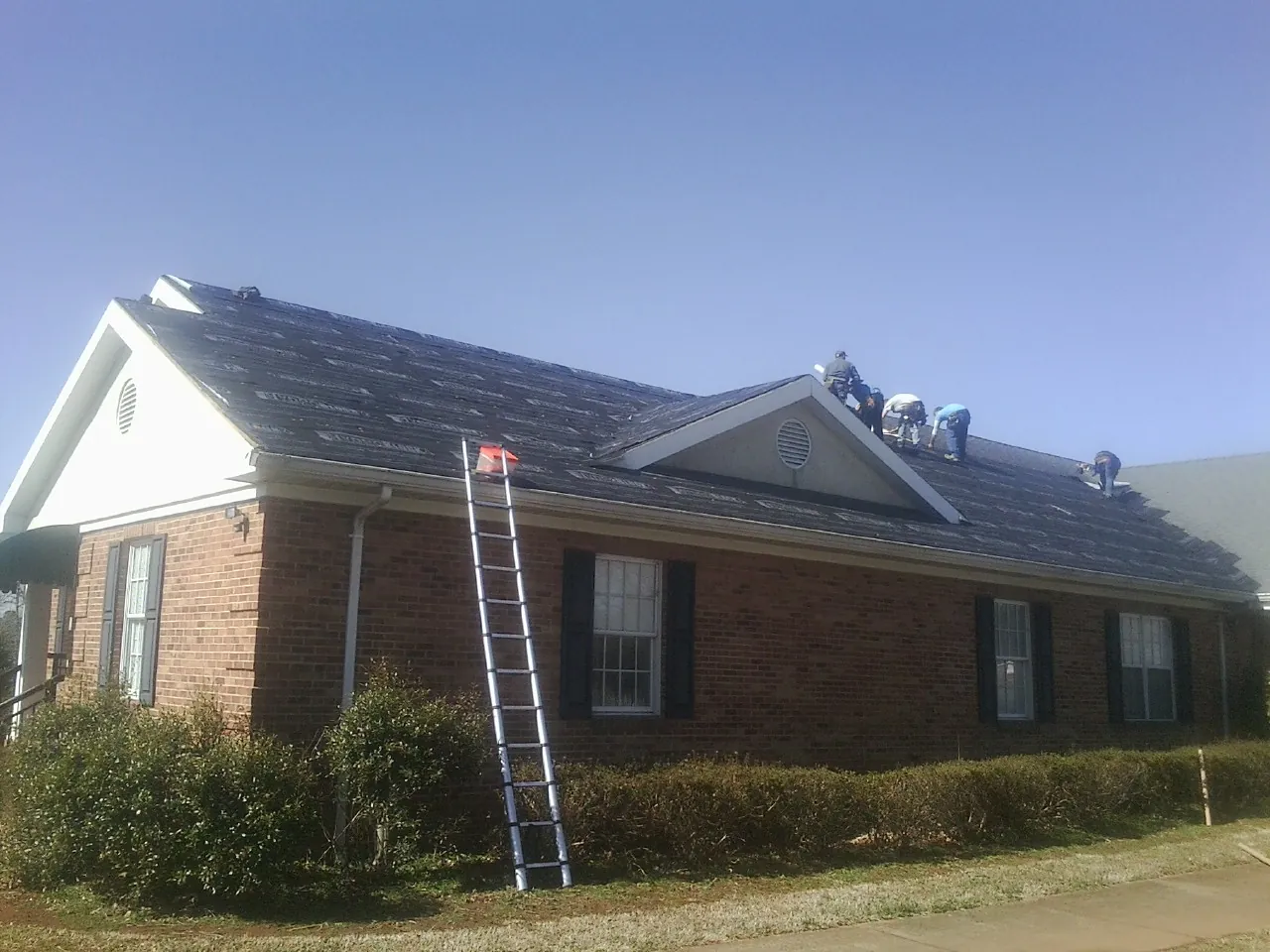 Crew tearing shingles off a brick ranch roof with a ladder set — Emergency Roof Repair work by our crew in Greenwich