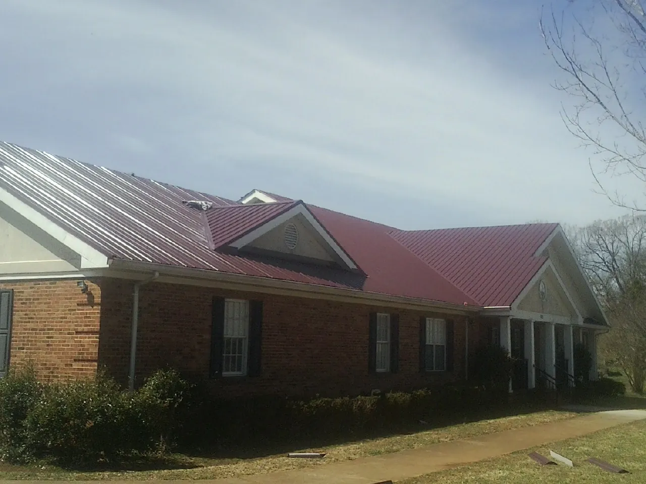 Red metal roof with gabled entries on a long brick building, from a Hail Damage Roof Repair job in Greenwich